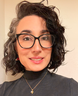 Justine Miracle, wearing glasses with curly hair, against a teal turtleneck